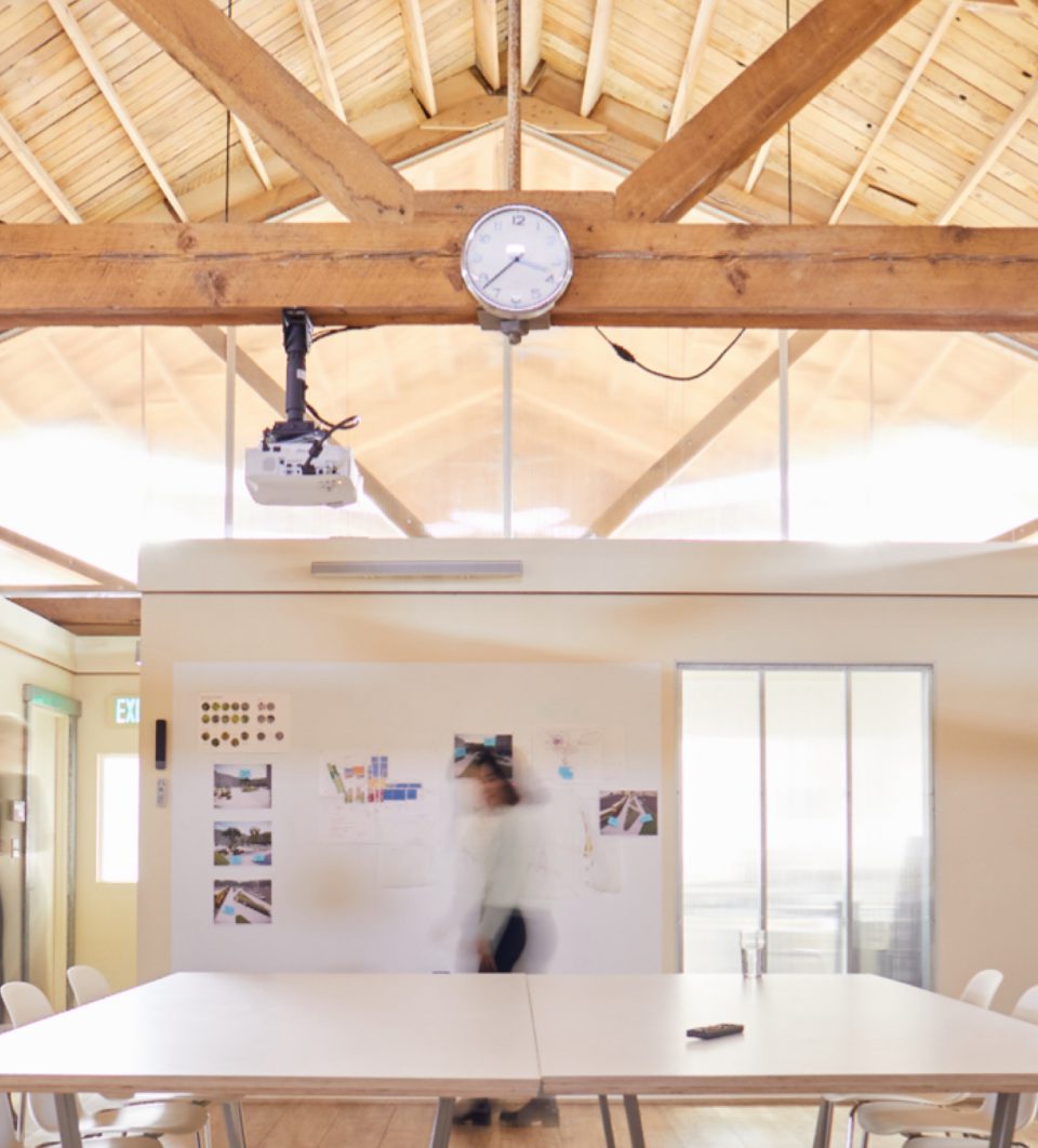 An office setting with a table and clock and time lapsed person walking by.